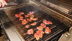 meat is being grilled on the grill by someone using tongs to cook them