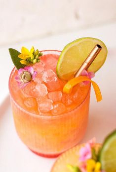 an orange cocktail garnished with flowers and lime