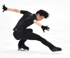 a male figure skating on an ice rink wearing black clothes and holding his arms out in the air