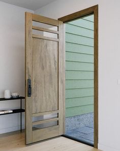 an open wooden door in front of a white wall and wood flooring with a shelf on the other side