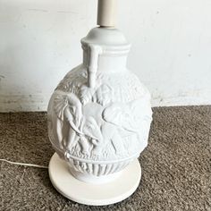 a white vase sitting on top of a table next to a light fixture with a cord in it