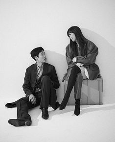 a man sitting next to a woman on top of a wooden bench in front of a white wall