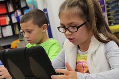 two children sitting at a table looking at an ipad