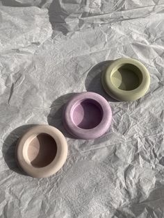 three different colored bowls sitting on top of a white sheet covered ground with wrinkled paper