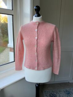 a pink cardigan sweater on a mannequin next to a window