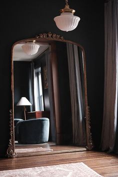 a large mirror sitting on top of a wooden floor next to a chair and lamp