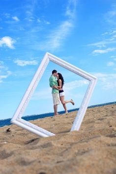 a man and woman are kissing on the beach in front of an empty photo frame