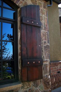 an old window with wooden shutters on the side of a stone building next to a brick wall