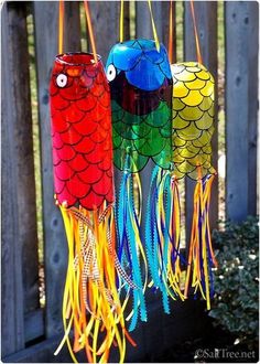 three colorful wind chimes hanging from a wooden fence