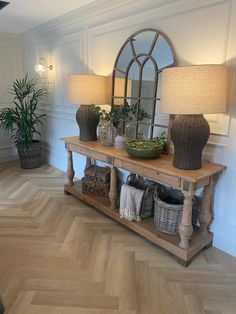 a wooden table topped with two lamps next to a mirror and potted plant on top of it