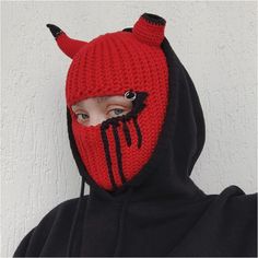 a person wearing a red and black knitted devil hoodie with horns on it