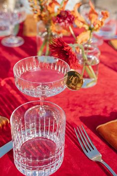 the table is set with glasses, silverware and flowers in vases on it