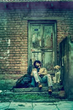 a man sitting on the steps with his dog next to him in front of an old brick building