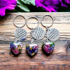 three heart shaped keychains with words on them and flowers in the back ground