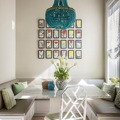 a dining room table and bench in front of a blue chandelier with pictures on the wall