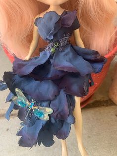 the doll is wearing a blue dress with purple flowers on it's skirt and butterfly brooch