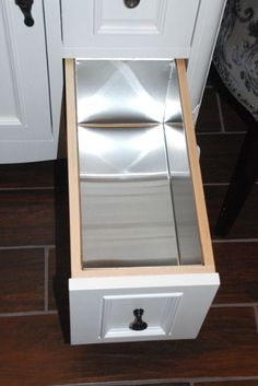 an open drawer in the middle of a kitchen floor with white cabinets and drawers on each side