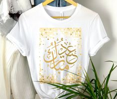 Celebrate Eid in style with our Eid Mubarak Shirt Gift. This t-shirt is the perfect present for Muslims to wear during the joyous occasion of Eid and Eid parties. Designed with elegance and cultural significance in mind, our Eid Mubarak Shirt features the phrase "Eid Mubarak" printed on a high-quality fabric. The stylish design and comfortable fit make it a must-have for your Eid festivities. Made from premium materials, this t-shirt offers both style and comfort. The soft fabric ensures a cozy Festive Short Sleeve Tops For Eid, Short Sleeve Tops For Eid Festivities, Casual White Top For Eid, Gold Short Sleeve Tops For Festivals, Gold Tops With Letter Print For Gifts, Festive Printed Tops For Eid, Gold Crew Neck Top As Gift, Graphic Tee Printed T-shirt For Gift, Graphic Tee Printed T-shirt As Gift