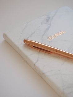 a gold pen sitting on top of a white marble book with the word journal written in gold