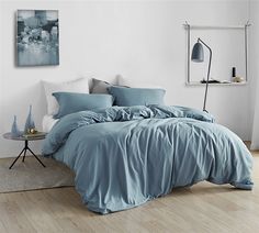 a bed with blue sheets and pillows in a white room next to a painting on the wall