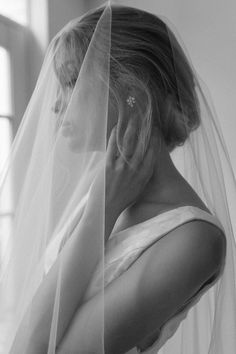 black and white photograph of a woman in wedding dress with veil over her head looking down