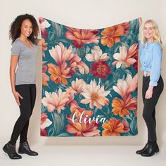 two women standing next to each other holding up a large blanket with flowers on it