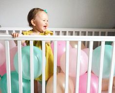 a baby in a crib surrounded by balloons