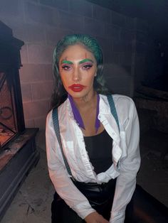 a woman with green hair and makeup sitting in front of a fire place