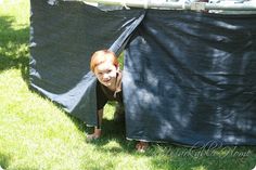 a young child is peeking out from behind a tarp in the grass with his mouth open