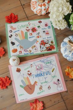 two thanksgiving cards on a wooden floor with fall leaves and pumpkins around the card