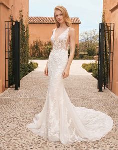 a woman in a white wedding dress standing on a stone walkway with an archway behind her