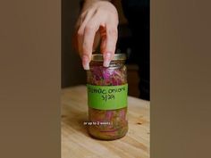 a hand reaching into a jar filled with pickled red onions on a wooden table