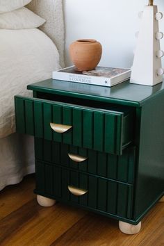 a green nightstand with two drawers and a book on top, in front of a white bed