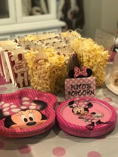 a table topped with pink plates filled with food and minnie mouse cupcakes on top of them