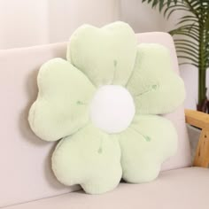 a green flower pillow sitting on top of a white couch next to a potted plant