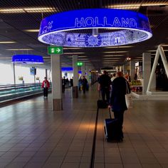 people are walking through an airport with their suitcases in hand and there is a sign that says holland above them