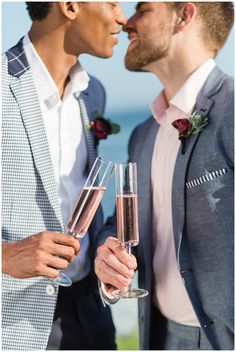 two men in suits are holding champagne flutes and looking into each other's eyes