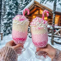 two people holding up glasses filled with pink and white sprinkles in the snow