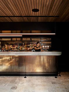 a woman sitting at a bar in front of bottles on the shelves and behind her