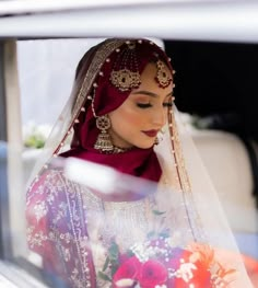 a woman wearing a veil and holding a bouquet in her hand while sitting in a car