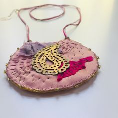 a pink purse with a gold and red design on the front is sitting on a white surface