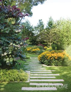 a garden with green grass, flowers and stepping stones on the ground in front of trees