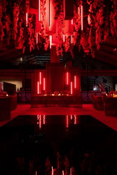 red lights are hanging from the ceiling above a pool in a dimly lit room with tables and chairs