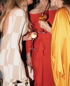 three women standing next to each other with wine glasses in their hands and one woman wearing a yellow dress