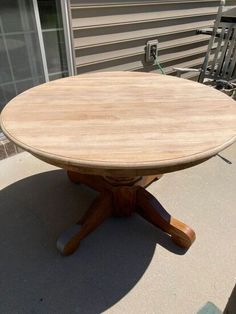 a round wooden table sitting on top of a cement floor next to a chair and window