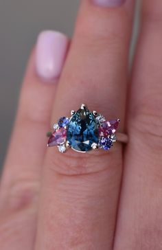 a woman's hand holding a three stone ring with blue and pink stones on it