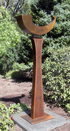 a large metal sculpture sitting in the middle of a park next to some bushes and trees