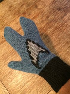 a blue knitted glove with a shark on it sitting on top of a wooden table