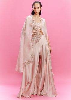 Dusky peach satin draped sharara with a blouse and a cape enhanced with the embellished lace. Peach Sharara, Dolly J, Bridal 2024, Draped Pants, Organza Cape, Cape Set, Lace Cape, Drape Pants, Contemporary Dresses