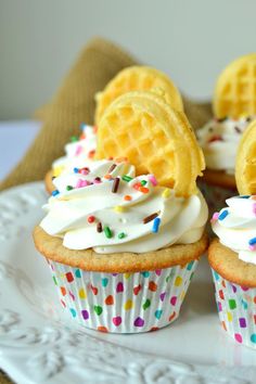 three cupcakes with white frosting and sprinkles on a plate